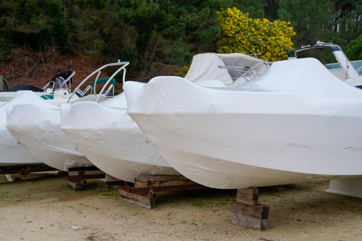  Boats covered with plastic white covers sit in a row. 