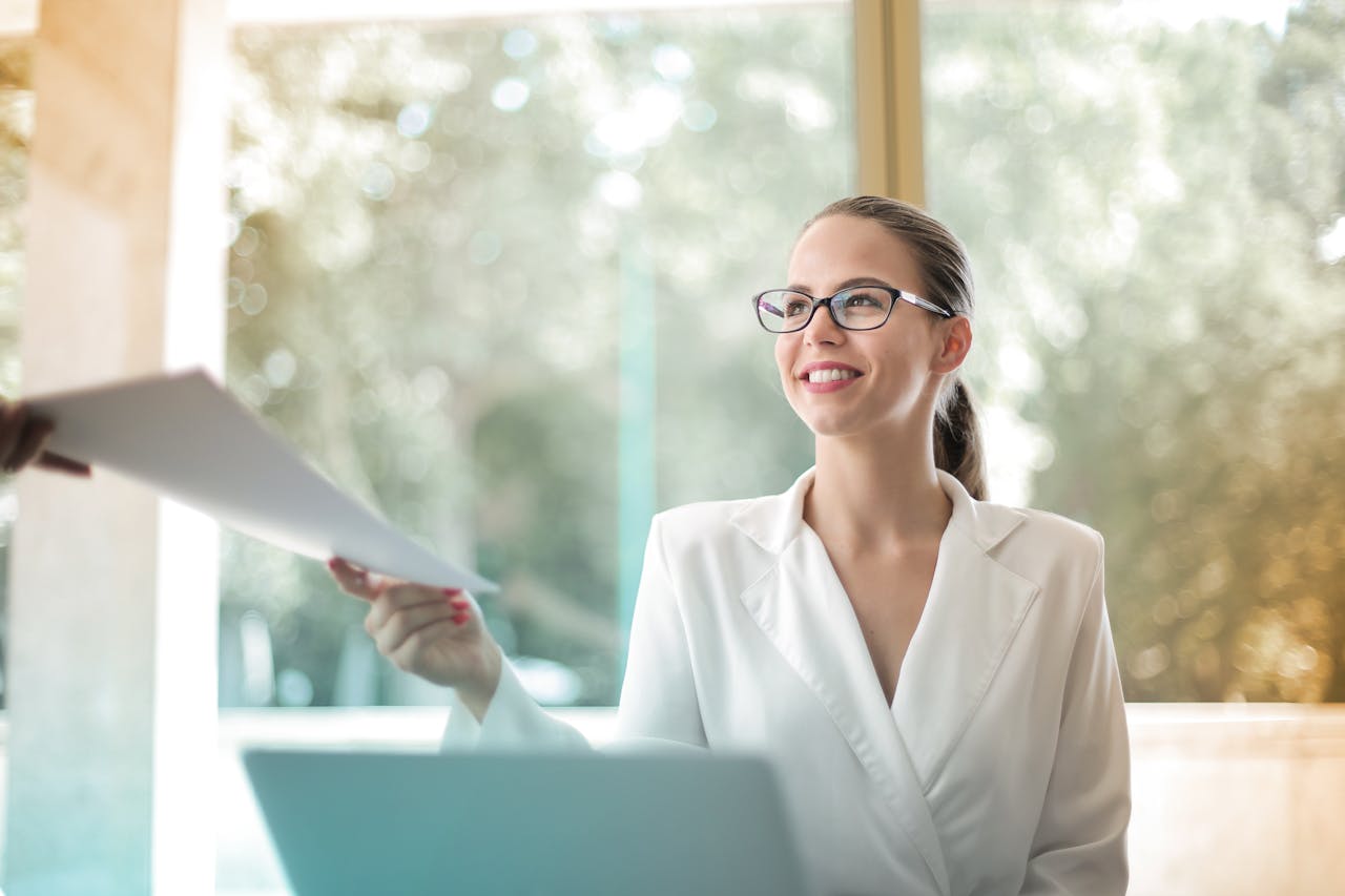 A businesswoman wearing glasses, confidently holding a piece of paper in her hand, ready for a meeting or presentation.