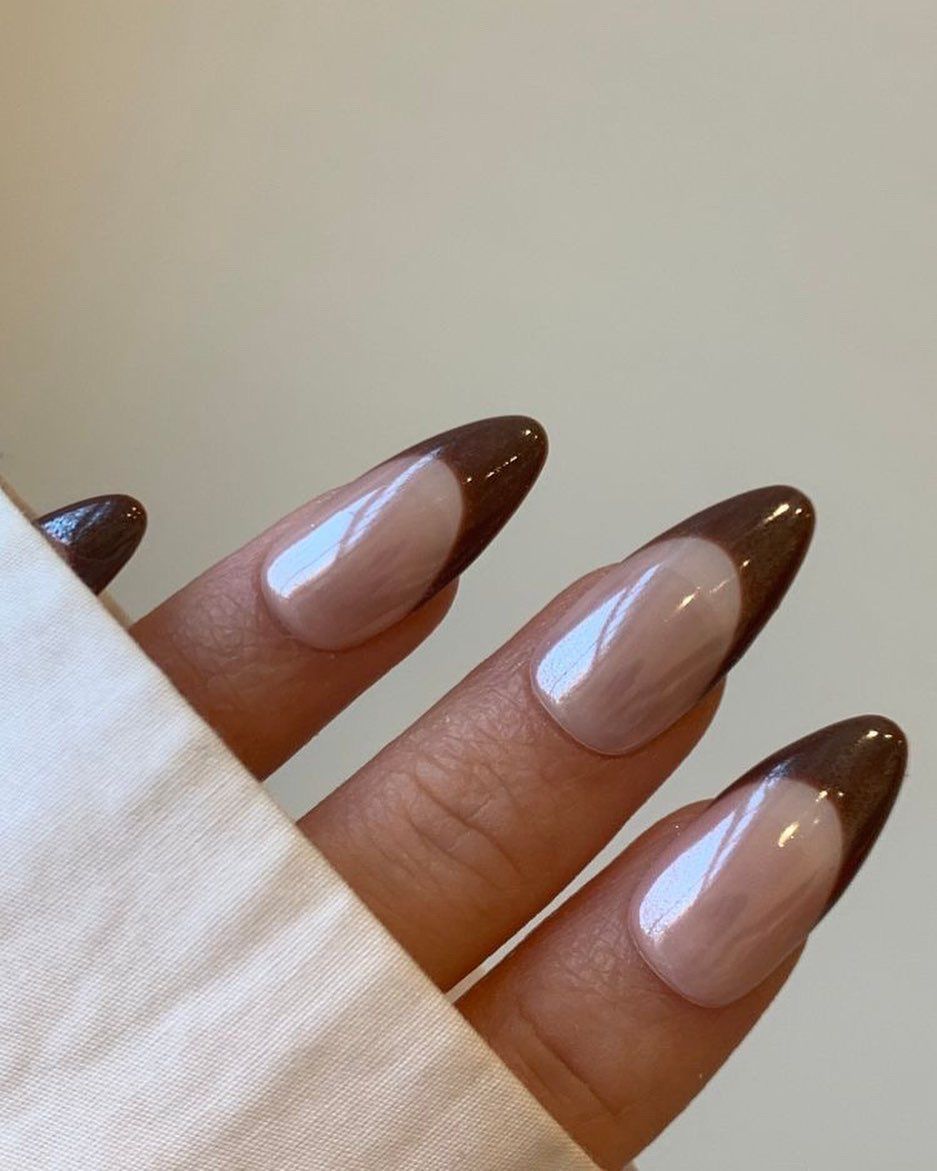  Long, almond-shaped nails with glossy taupe polish and brown tips.