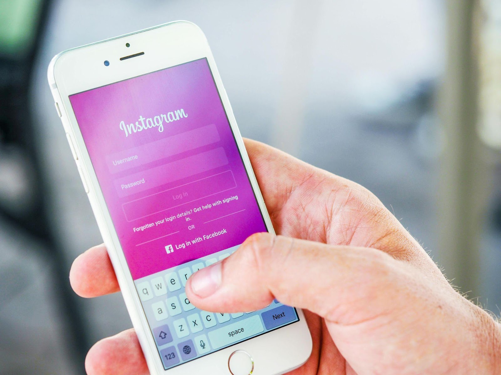 A person holding a smartphone with the Instagram login screen displayed, focusing on the phone with a blurred background