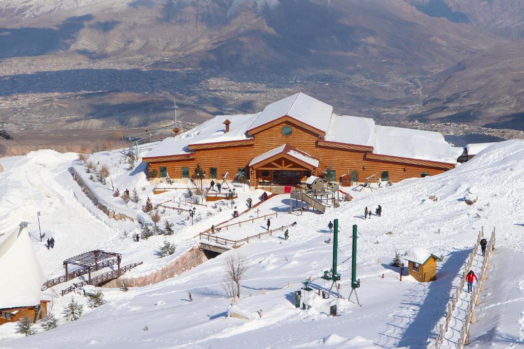 Scenic view of Korek Mountain Resort in Erbil, Iraq, with snowy slopes, a wooden lodge, and skiers enjoying the winter activities, set against a mountainous backdrop.