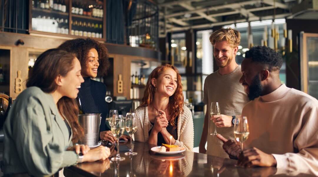 A group of friends enjoying drinks and dessert at a bar, smiling and chatting together.