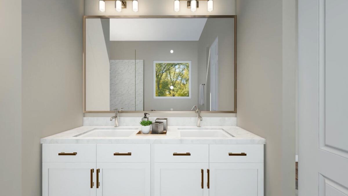 The white vanity includes double sinks and a large framed mirror brightened by glass sconces.