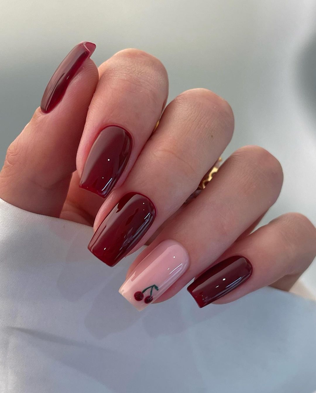 Close-up of a hand with polished nails, varying shades of red, one with a cherry design.

