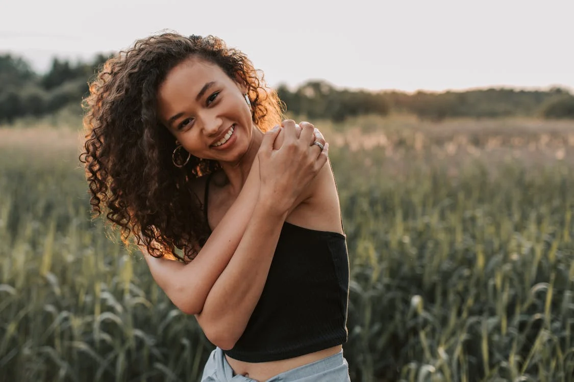 A woman in a field, giving herself a hug. 
