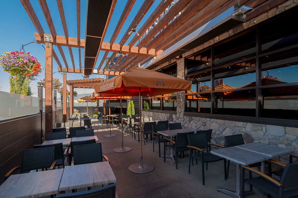 View of Milestone's patio with a wooden pergola, tables and chairs, and orange umbrellas with their logo. 