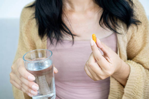 A woman holding a berberine capsule in one hand and a glass of water in the other, preparing to take her daily supplement for overall health support.