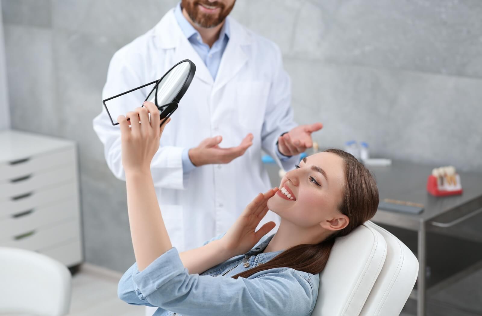 A young woman admires her new dental crown in a mirror.