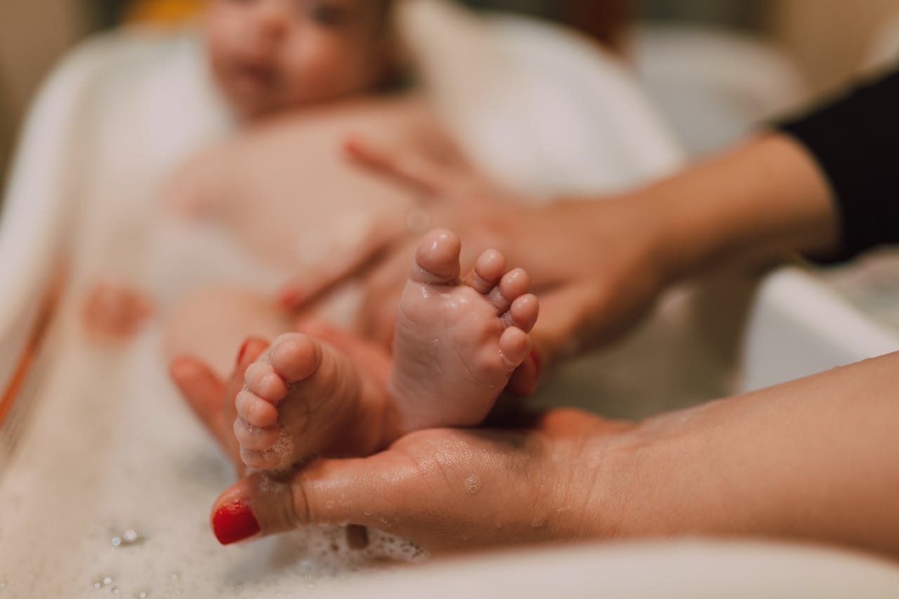 Person washing a baby’s feet in a bath // Healthier Baby Today