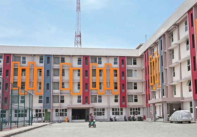 Tampak depan bangunan rumah susun sederhana milik negara (Rusunawa) dengan desain warna-warni merah, oranye, dan abu-abu serta area terbuka di tengah.