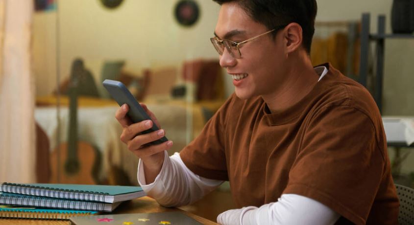 A man wearing glasses while holding a phone and smiling