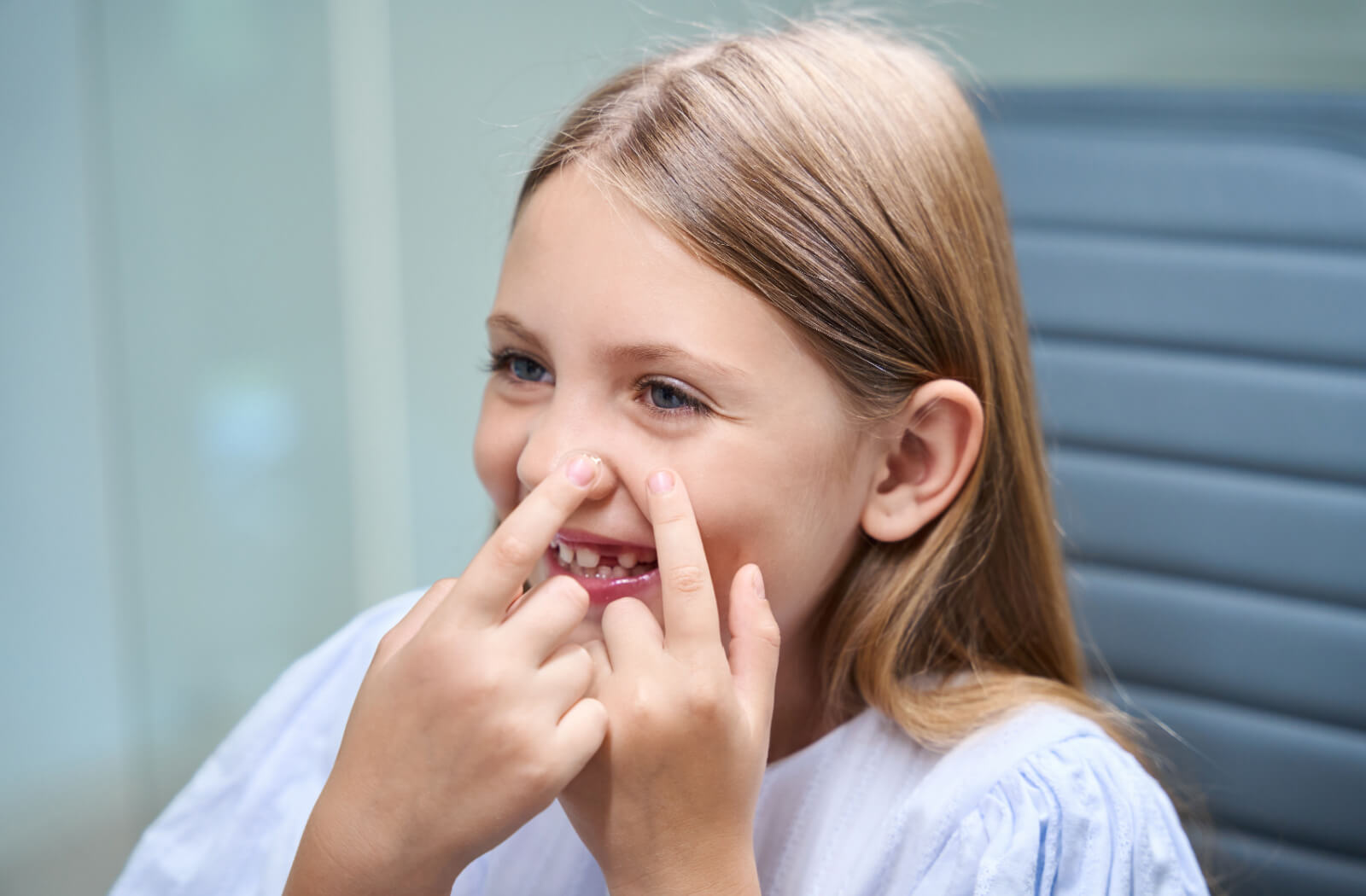 A young child smiling in the bathroom and carefully using both hands to put a contact lens into their left eye.
