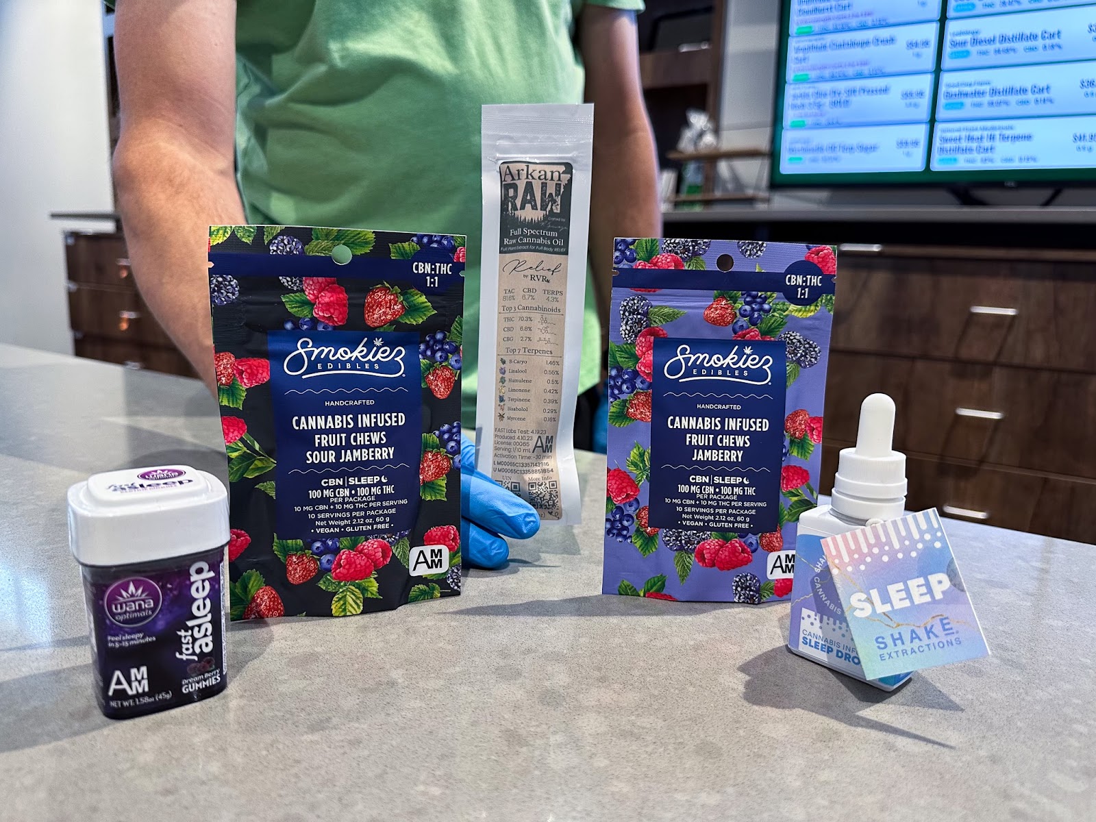 Longtime budtender of The Source cannabis dispensary in Rogers, Arkansas, Shaun Forrester shows off popular edible options to help with sleep including, WANA’s Fast Asleep gummies, Smokiez 1:1 THC:CBN Jamberry gummies, ArkanRAW full-spectrum cannabis oil, and Shake Extractions sleep tincture.