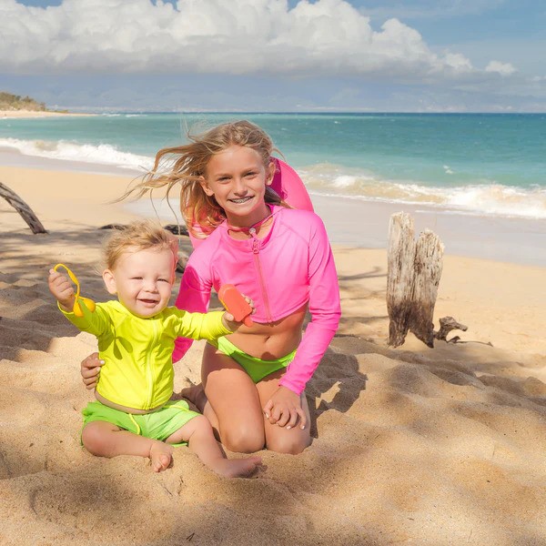 Brother and sister in SwimZip neon green, pink, and yellow swimwear at the beach—What is the best swimsuit color for safety?