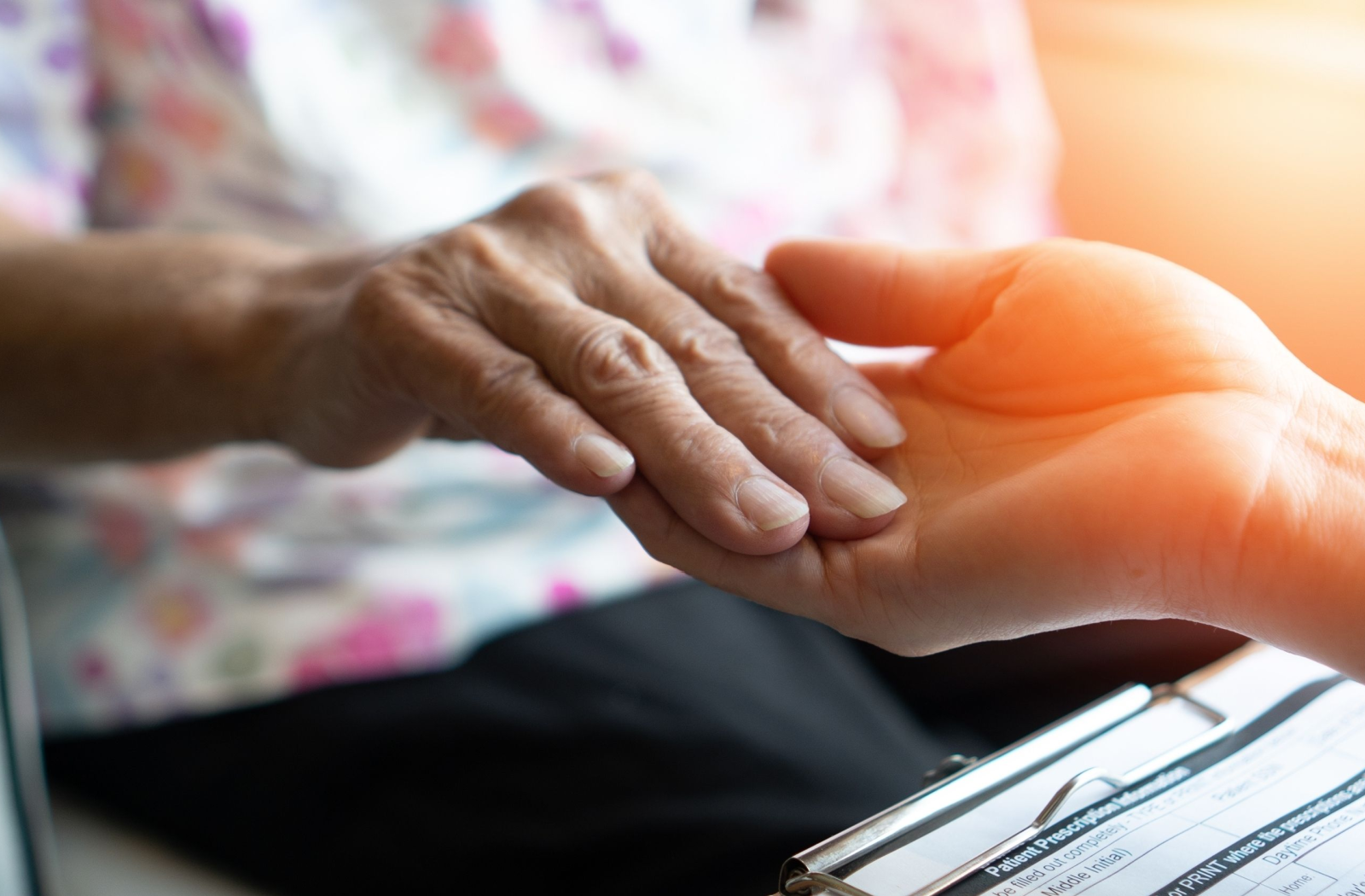 An adult child tenderly holds their senior parent's hand.