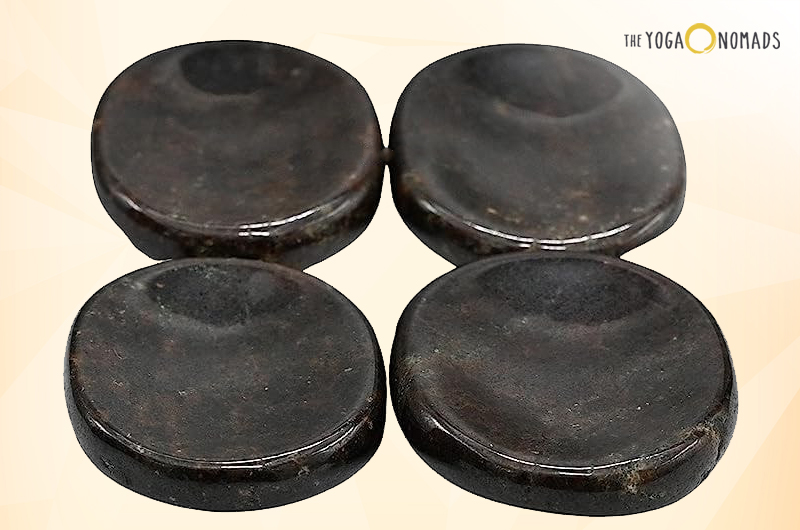 Four circular, dark-colored objects that appear to be flat stones or weights, possibly used for yoga or fitness purposes, placed on a light-colored surface.