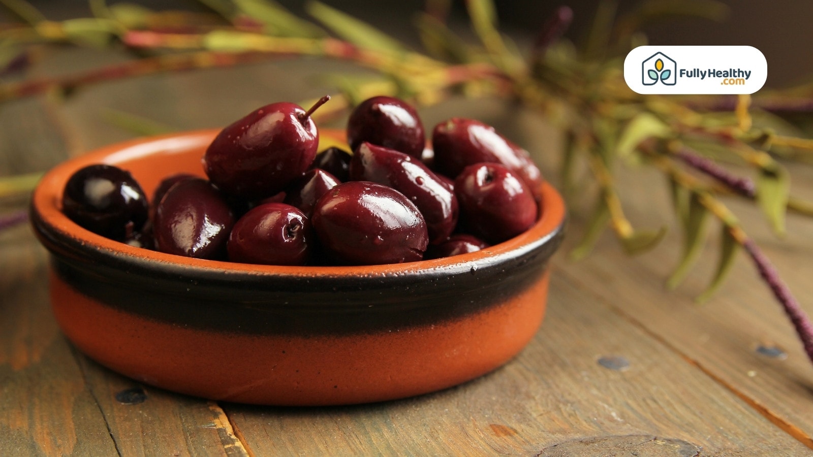 Kalamata olives in ceramic bowl with rustic wooden background
