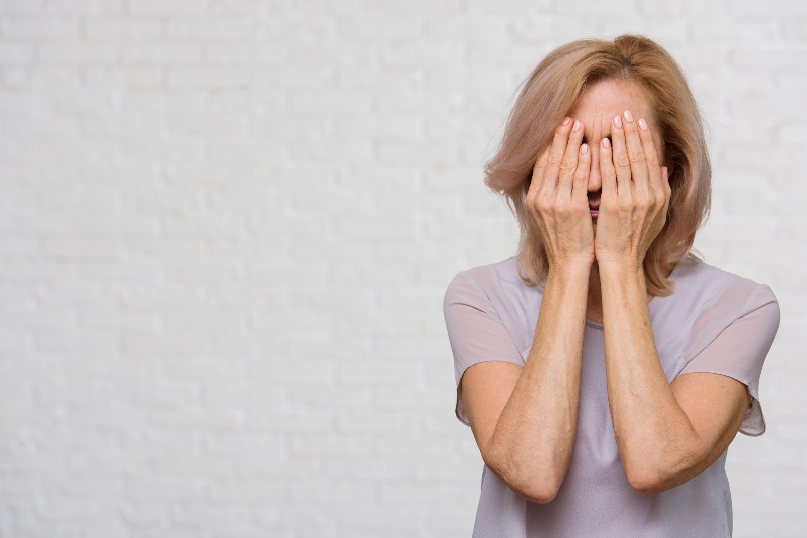 An upset older woman covering her face while crying | Source: Freepik