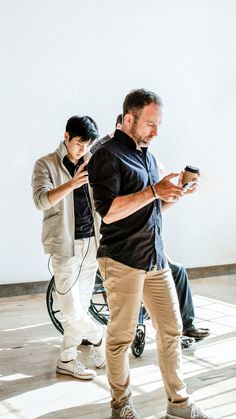 This contain: two men standing next to each other while looking at their cell phones in the same direction