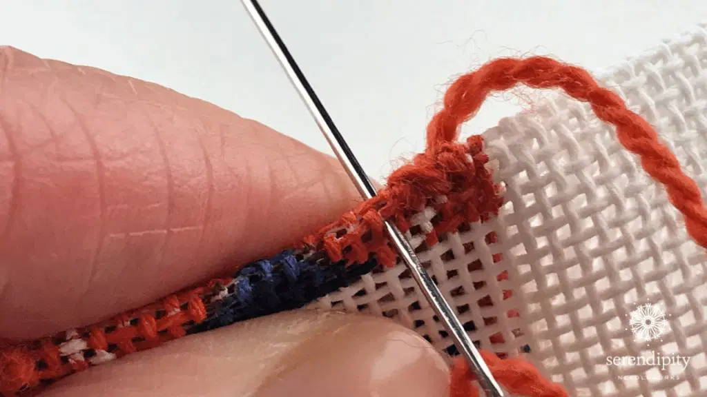 Close-up of hands stitching a binding stitch needlepoint edge with a tapestry needle
