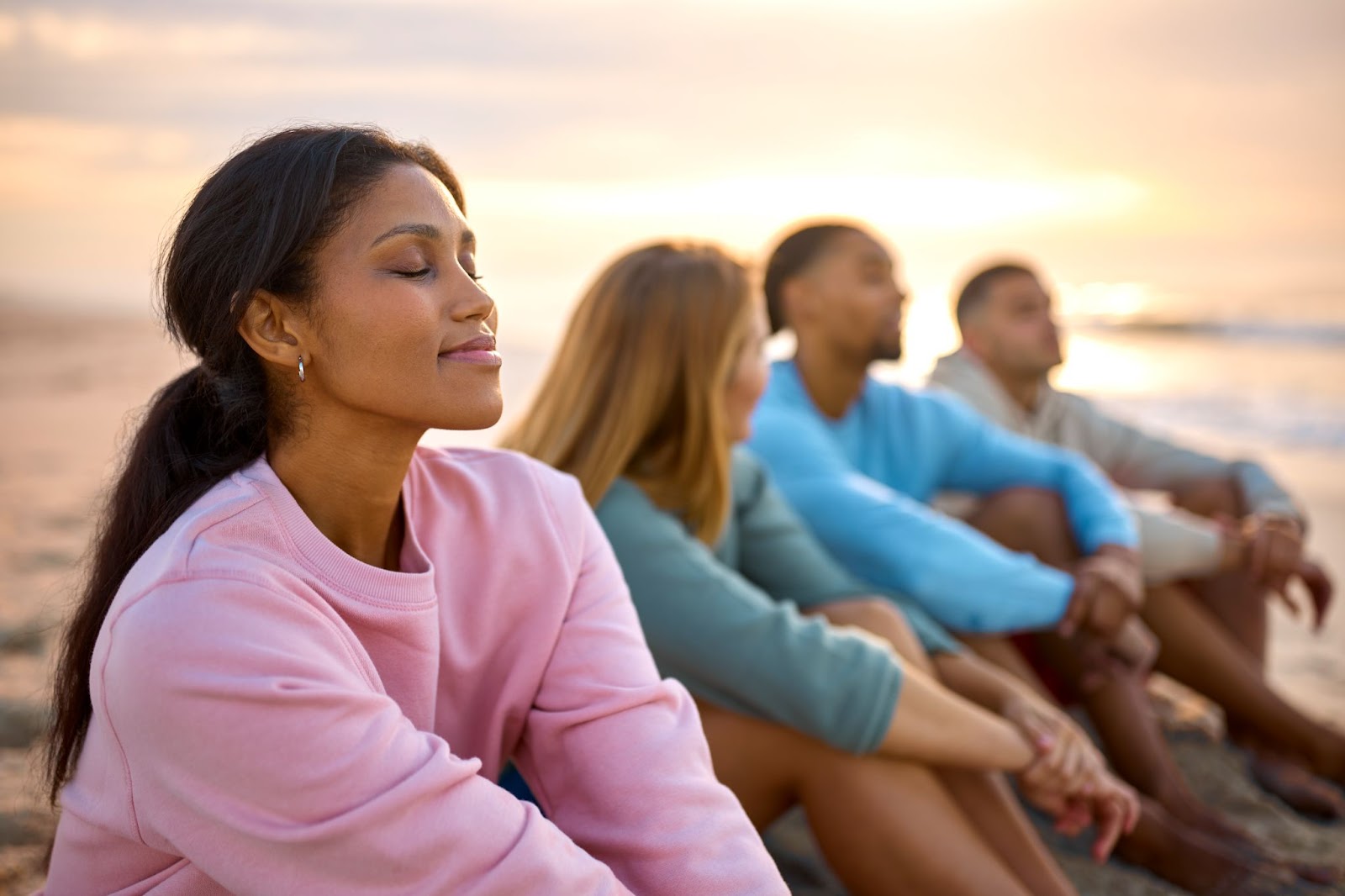 Woman with her eyes closed and relaxed next to a group of friends on the beach at sunset. 