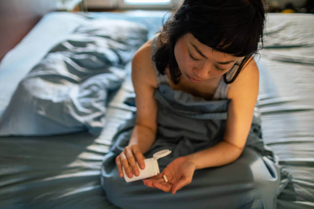 A woman sitting on her bed, taking magnesium and melatonin supplements before bedtime.