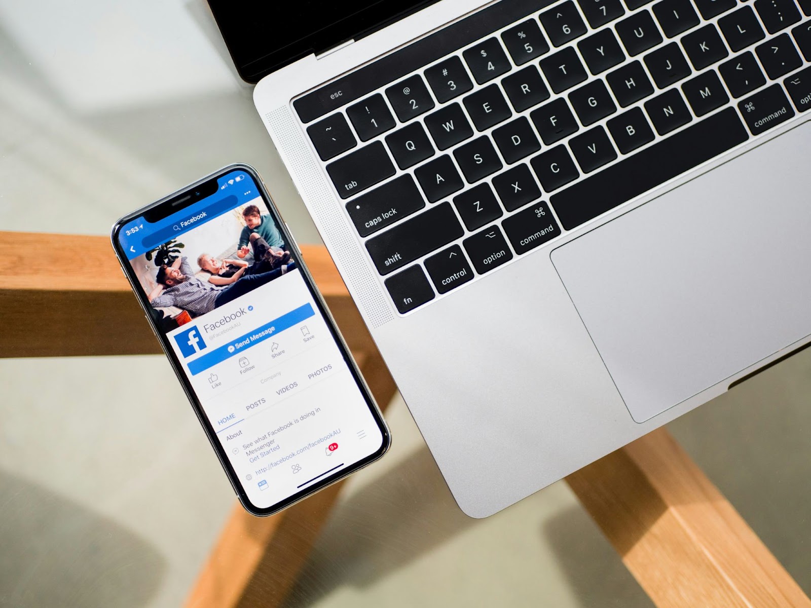 Smartphone displaying Facebook app next to a laptop on a wooden table