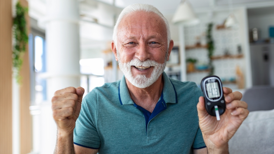 A smiling elderly man proudly showing a glucometer displaying a blood sugar level within the normal range.