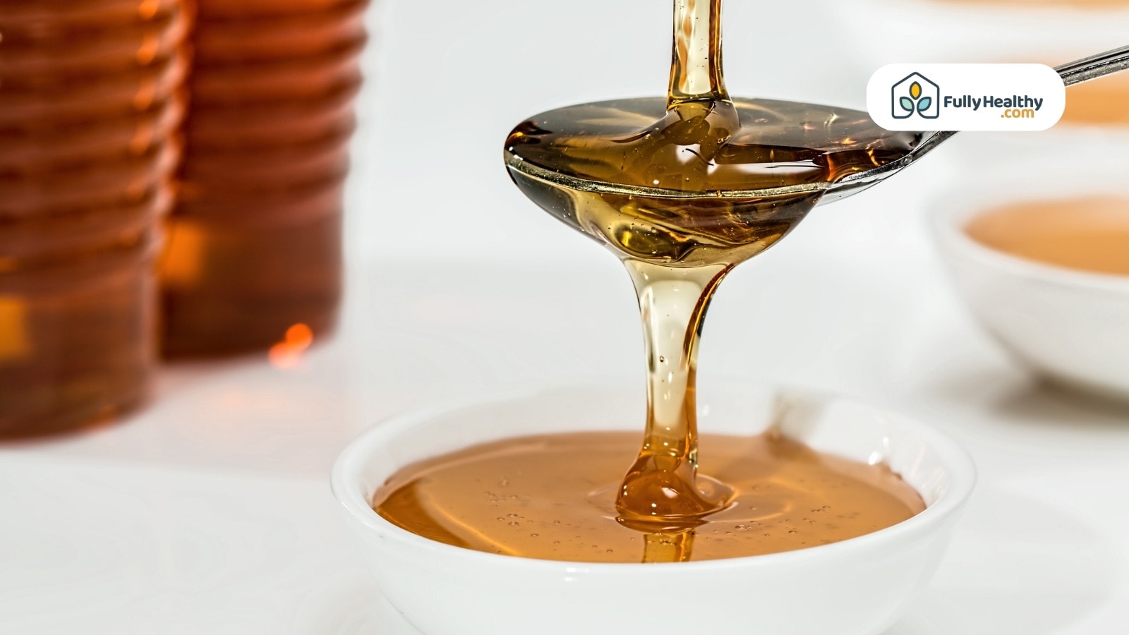 Golden honey flowing from spoon into a white ceramic bowl