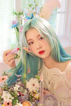 This contains an image of: Yerin Baek wearing a white gown with a mixture of off white and sky blue hair with flowers around her 