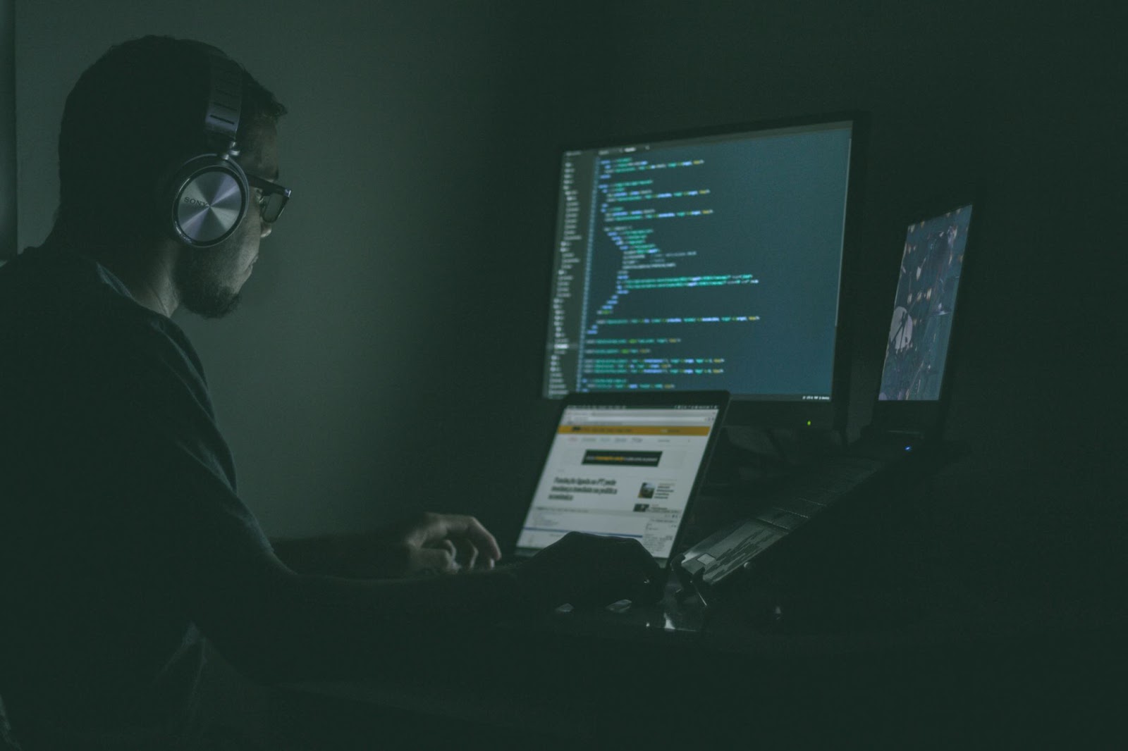 A hacker works in a dark room, surrounded by screens filled with code and cybersecurity tasks.