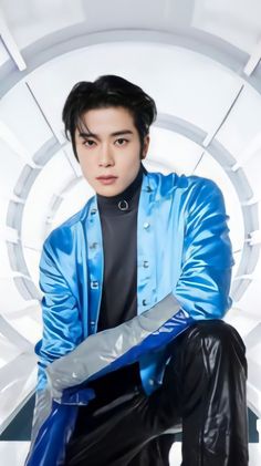 A picture of NCT's Jaehyun wearing a blue jacket and a black inner shirt with a black trouser and kneeling down with one of his leg on the ground 