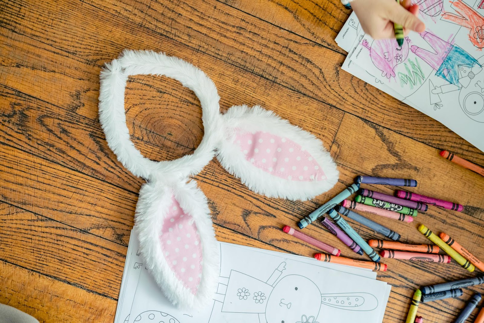 Kid's crafting setup with bunny ears, crayons, and colorful drawings on wooden floor.