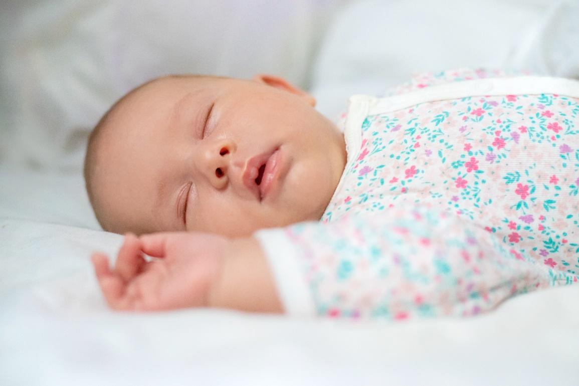 A baby sleeping on a white blanket

Description automatically generated