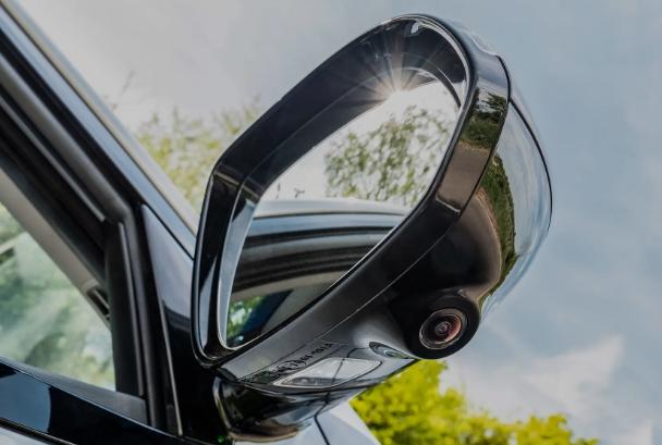 A modern car's side mirror with an integrated 360-degree view camera built into the underside of its housing.
