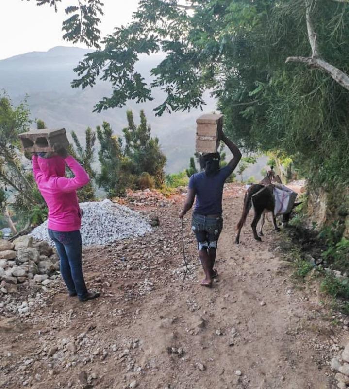 Two people carrying bricks on their heads

Description automatically generated