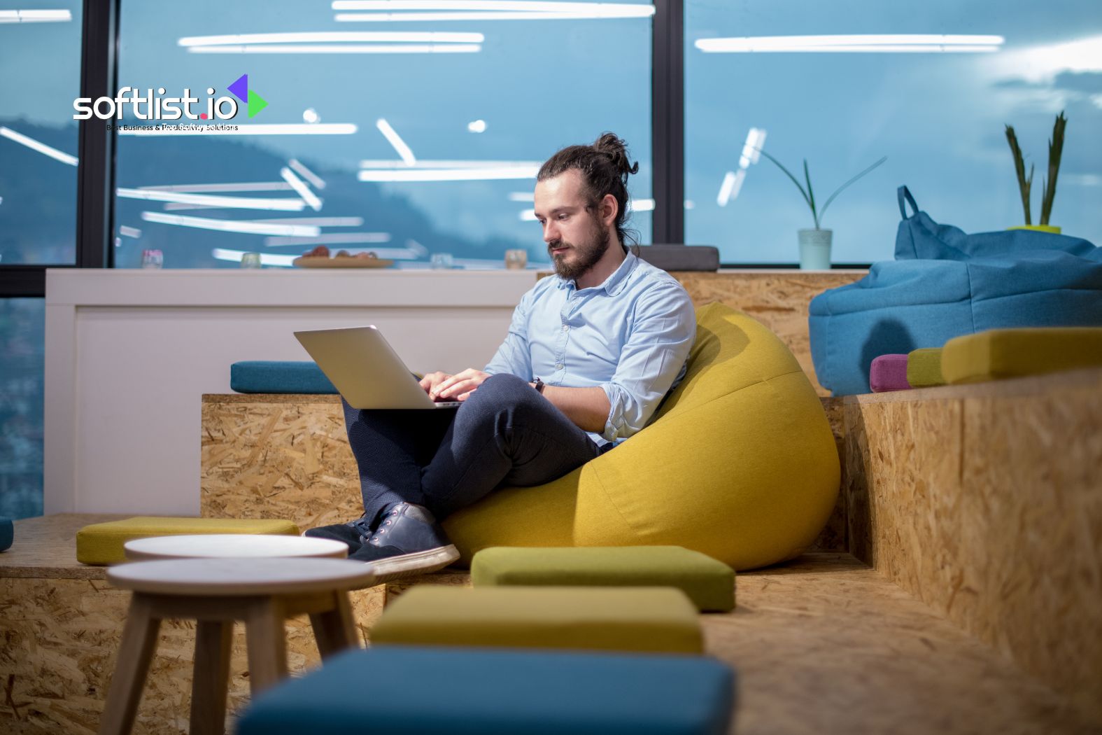 A man sitting on a yellow beanbag using a laptop in a modern office