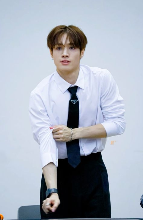 A photo of Jay Chang wearing a white shirt and black tie with his hands on his hips while standing in front of a desk