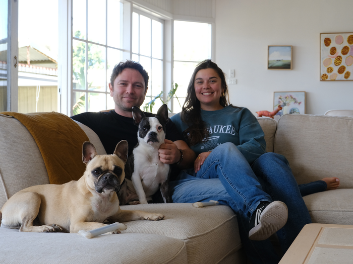 The author and her partner sitting on a couch with two frenchies, smiling at the camera.