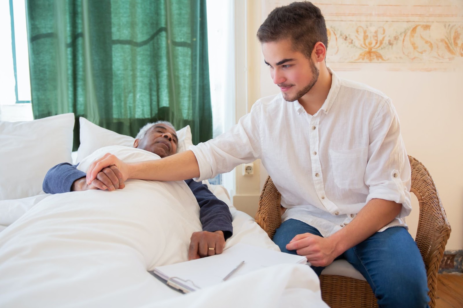 A picture of an inpatient facility caregiver with his hands on a patient's hand while the patient is in bed