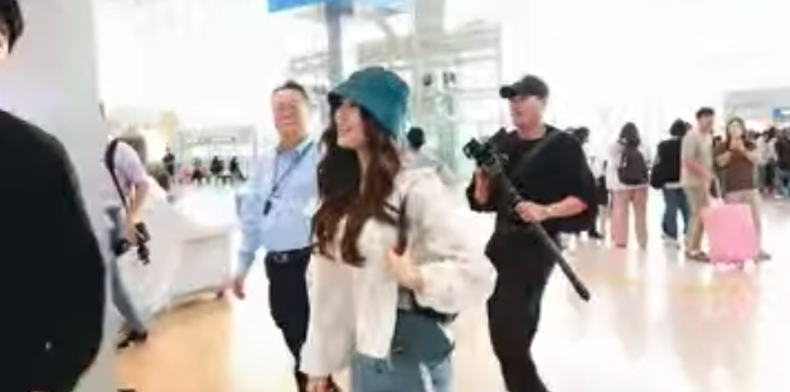 A picture of Olivia Marsh wearing a white jacket and a vest inside of it and a green cap at the airport