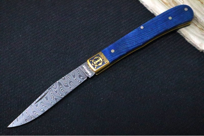 An image showing a Boker folding knife with a patterned Damascus-style blade. The knife features a blue handle and metallic bolsters near the pivot area.