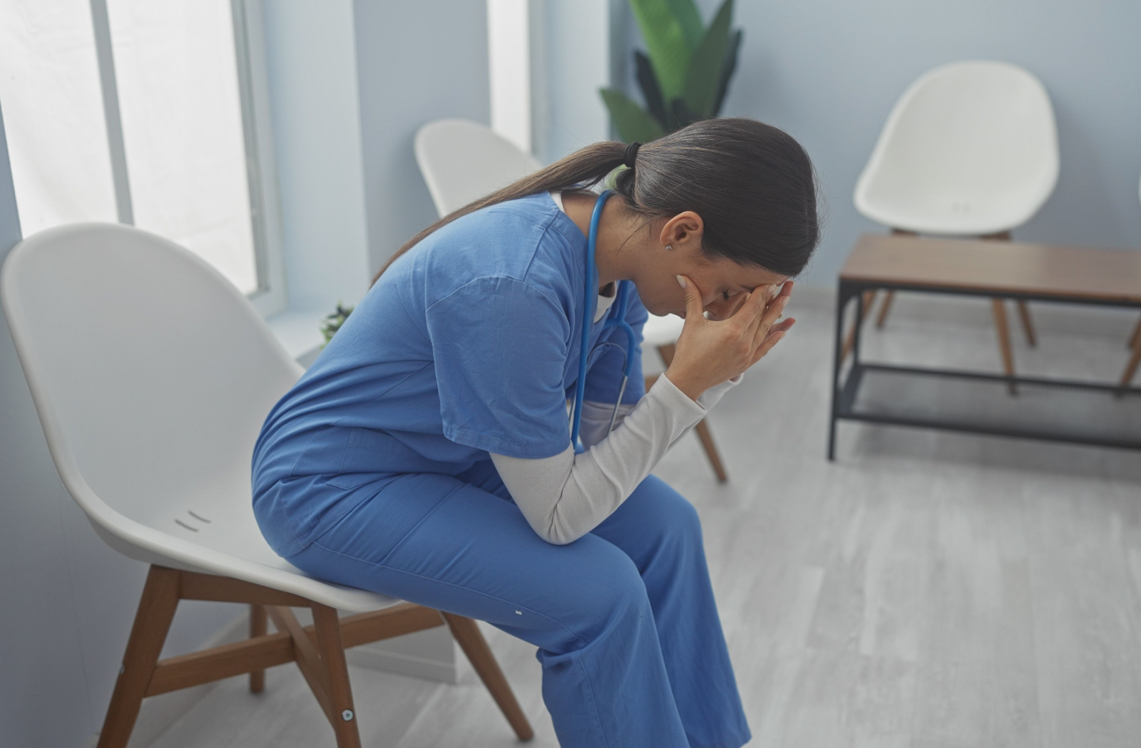 An exhausted nurse sits in a white chair, head in their hands.