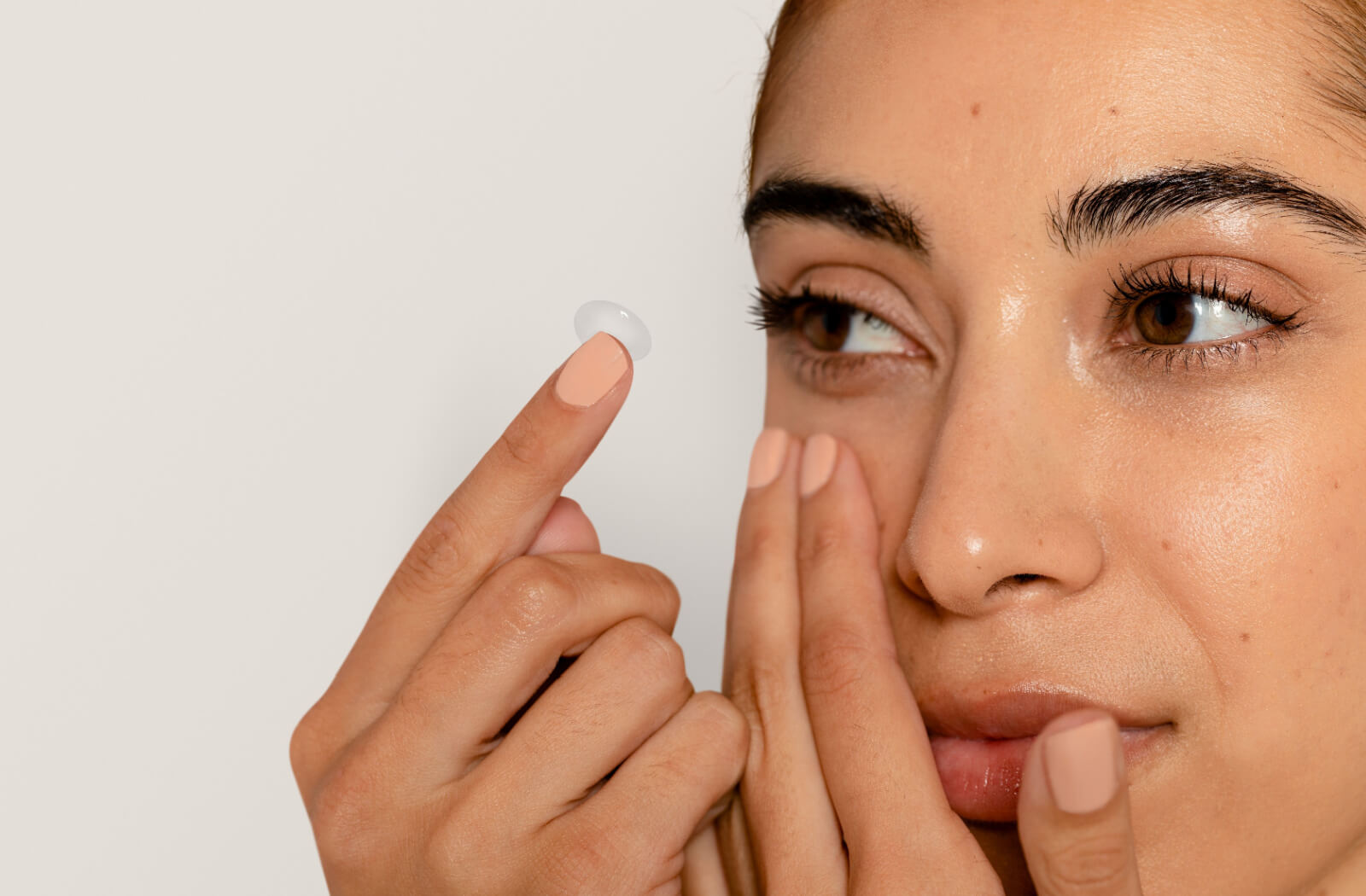 A young adult smiling while carefully inserting a scleral contact lens into their right eye.