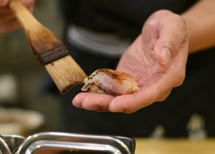 A piece of sushi being gently brushed with soy sauce.