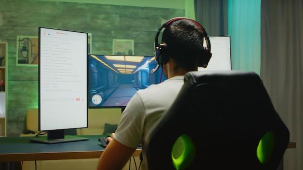 Free photo back view of professional gamer streaming his competition on triple monitor setup with two streaming chats open