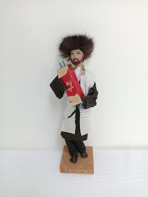 This doll depicts an orthodox Jewish Rabbi holding a Torah