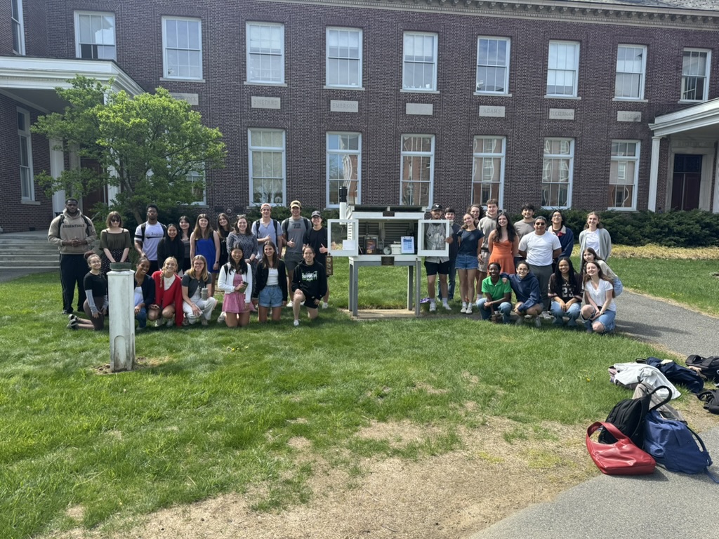 The students and Dr Fein stand around the campus weather station on a sunny day