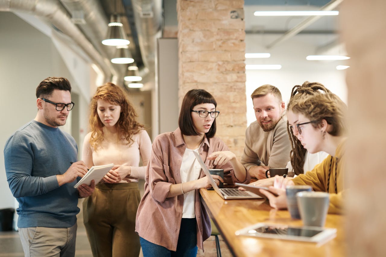 A diverse group of people gathered around a table, engaged with a tablet, sharing ideas and collaborating together.