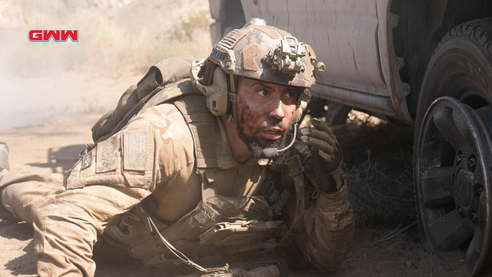 Raymond crouching beside vehicle in a dusty environment, looking stressed.